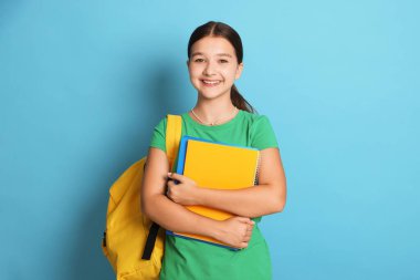 Sırt çantası ve açık mavi arkaplan üzerine not defterleri olan genç kız.