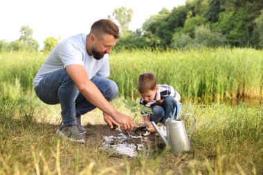 Baba ve oğlu dışarıda toprağa ağaç dikiyorlar.