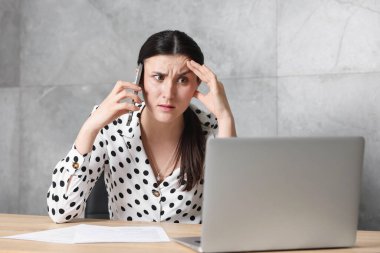 Evrakları ve dizüstü bilgisayarı olan genç bir iş kadını ahşap masadaki birine şikayet ediyor.