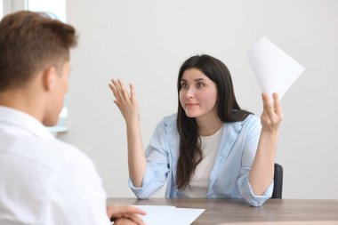 Genç bir kadın içerideki ahşap masadaki adama şikayette bulunuyor.