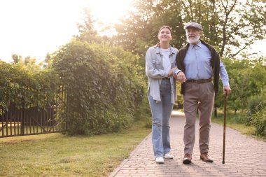 Gülümseyen bakıcı dışarıda bastonuyla yaşlı bir adamı destekliyor. Metin için boşluk
