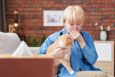 Yaşlı kadın evdeki kanepede kedisiyle alerji geçiriyor.