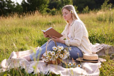 Bir buket kır çiçeğiyle çayırda kitap okuyan bir kadın.