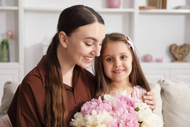 Anne ve kızı evdeki kanepede bir buket güzel şakayıkla