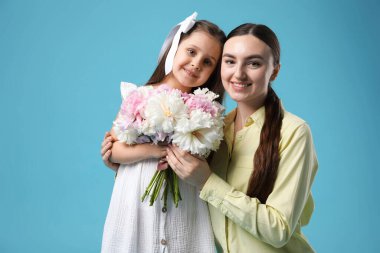 Anne ve kızı açık mavi arka planda bir buket güzel şakayıkla