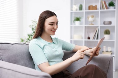 Evdeki koltukta modern tablet kullanan genç bir kadın.