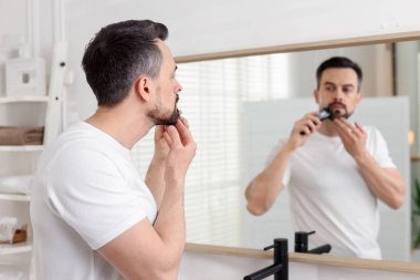 Yakışıklı adam aynanın yanında tıraş makinesiyle tıraş oluyor, seçici bir odak noktası var.