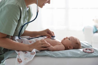 Klinikteki masada steteskopla bebeği muayene eden çocuk doktoru.