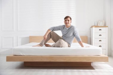 Genç adam evinde yumuşak bir yatakla yatakta oturuyor.