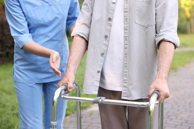 Hemşire dışarıda yürüyen çerçeve kullanan yaşlı adama yardım ediyor, yakın plan.