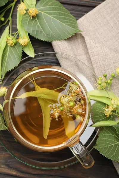Fincanda taze ıhlamur çayı ve koyu ahşap masada çiçekler.