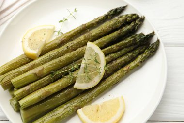 Beyaz ahşap masada limon ve kekik ile servis edilen lezzetli pişmiş kuşkonmaz.