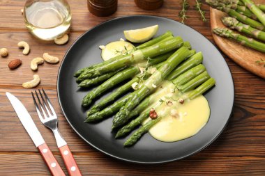 Ahşap masada limon ve sos ile servis edilen lezzetli pişmiş kuşkonmaz, yakın plan.