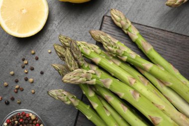 Taze çiğ kuşkonmaz mızrakları, limon ve baharatlar siyah masada, düz yerde.