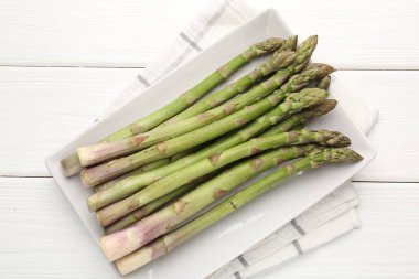 Beyaz ahşap masada taze çiğ kuşkonmaz mızrakları.