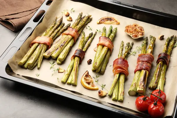 Pastırma, domates ve baharatlarla pişirilmiş lezzetli kuşkonmaz. Gri masada, yakın plan.