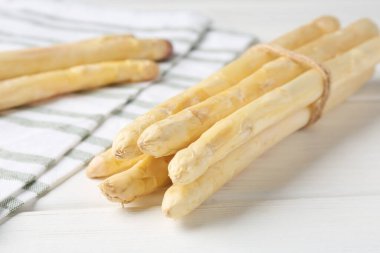 Beyaz ahşap masada çiğ kuşkonmaz mızrakları, yakın plan.