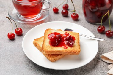 Lezzetli kiraz reçelli tostlar, çay ve taze meyveler gri masada, yakın plan.