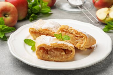 Lezzetli elmalı turta parçaları pudra şekeri, nane ve meyveler gri masada, yakın plan.