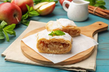 Lezzetli elmalı turta parçaları pudra şekeri, nane, meyve ve tarçın ile açık mavi ahşap masa, yakın plan