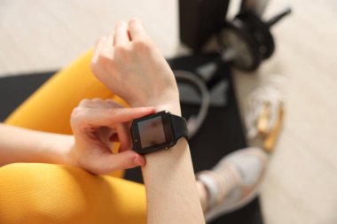 Kadın spor salonunda spor yaparken takip cihazını kontrol ediyor, yakın plan.