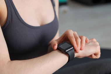 Kadın spor salonunda spor yaparken takip cihazını kontrol ediyor, yakın plan.