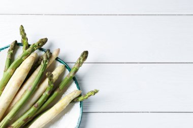 Beyaz ahşap masada farklı çiğ kuşkonmaz mızrakları, üst manzara. Metin için boşluk