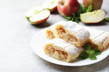 Lezzetli elmalı turta parçaları pudra şekeri ve açık gri masada nane şekeri, yakın plan.