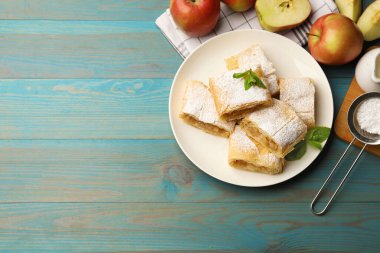 Pudra şekerli, nane şekerli ve açık mavi ahşap masada meyveli elmalı turta. Metin için boşluk