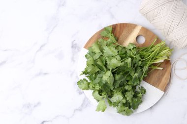 Taze aromatik kişniş, beyaz mermer masa üzerinde kesim tahtası ve iplik, üst manzara. Metin için boşluk