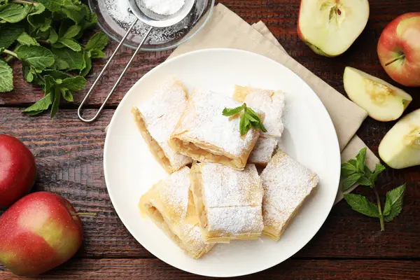 Lezzetli elmalı turta parçaları pudra şekeri, nane ve ahşap masa üzerinde meyve, düz uzanmış