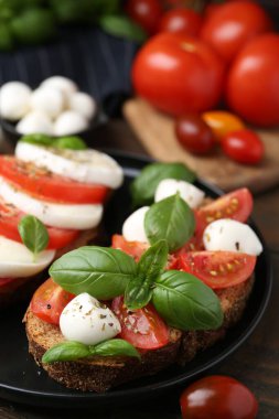 Peynirli, domatesli, fesleğenli ve baharatlı lezzetli sandviçler ahşap masada, yakın plan.