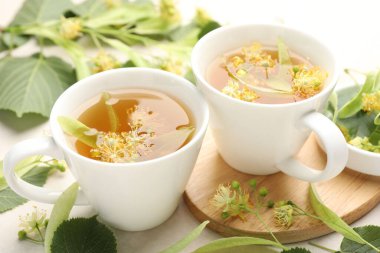 Fincanlarda taze ıhlamur çayı ve beyaz masada çiçekler, yakın plan.