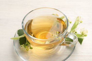 Fincanda taze ıhlamur çayı ve beyaz ahşap masada çiçekler, yakın plan.