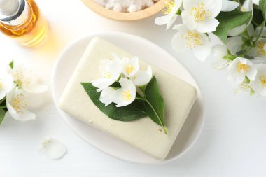 Sabun çubuğu, deniz tuzu, temel yağ ve yasemin çiçekleri beyaz ahşap masa üzerinde, düz yatıyordu.