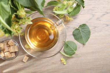 Fincanda nefis ıhlamur çayı, küp şekerler, yapraklar ve çiçekler ahşap masada, düz uzanmış