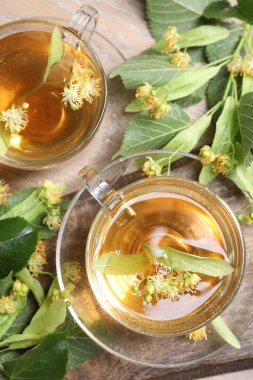 Fincanlarda nefis ıhlamur çayı, ahşap masada yapraklar ve çiçekler.