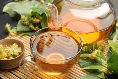 Lezzetli ıhlamur çayı, çaydanlık, yapraklar ve çiçekler koyu masada, yakın plan.