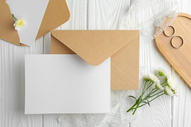 Düğün davetiyeleri, zarflar, gümüş yüzükler, çiçekler ve kurdele beyaz ahşap masa, düz uzanma