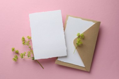 Düğün davetiyeleri, zarf ve dalları pembe arka planda, düz uzanmış