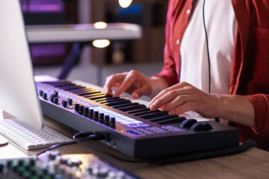 İçerideki ahşap masada MIDI klavyesiyle çalışan adam, yakın plan.