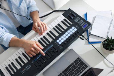 Beyaz masadaki MIDI klavyesiyle çalışan bir adam.