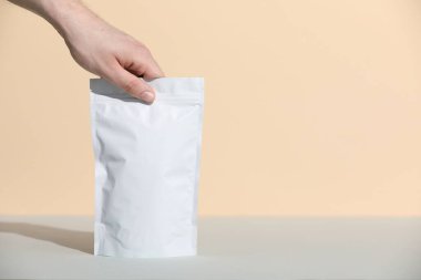 Gri masadaki boş fermuarlı stand-up çantasını bej arka planda tutan kadın, yakın plan. Metin için boşluk