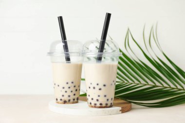 Plastik bardakta sütlü çay ve bej masada yeşil yapraklar.