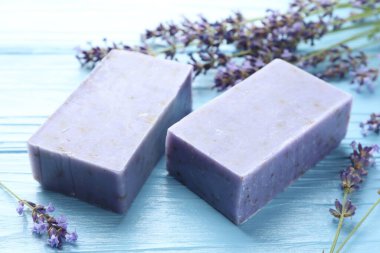 Aromatik sabun barları ve lavanta çiçekleri açık mavi ahşap masada, yakın plan.