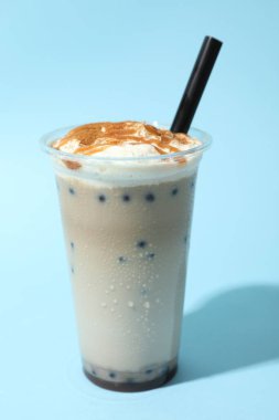 Açık mavi zemin üzerinde plastik bardakta lezzetli süt köpüğü çayı