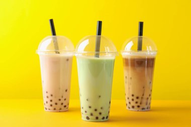 Sarı arka planda plastik bardakta lezzetli süt köpüğü çayı.