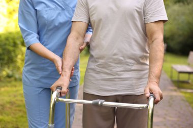 Hemşire dışarıda yürüyen çerçeve kullanan yaşlı adama yardım ediyor, yakın plan.