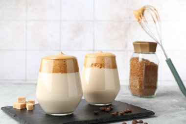 Bardakta lezzetli dalgona kahvesi, esmer şeker, fasulye, çırpı ve granüller gri masada, yakın plan.