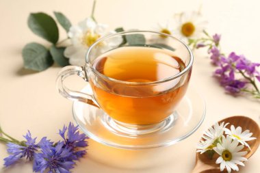 Cam fincanda aromatik bitki çayı ve bej arka planda farklı çiçekler, yakın plan.